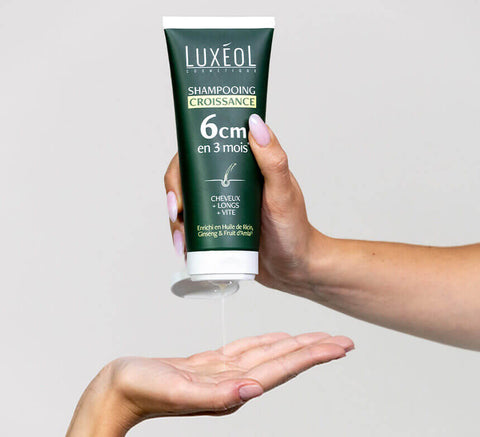 Shampoo tube held in hand against neutral background.