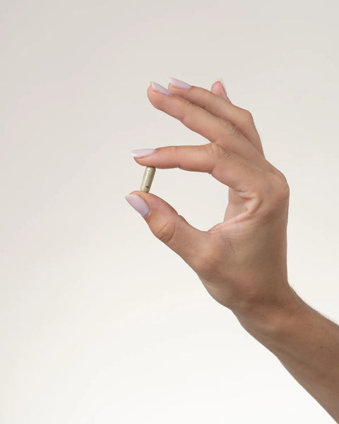 Hand holding a small capsule against a plain background