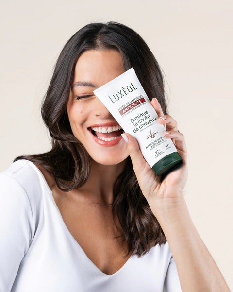 Woman holding a Luxeol hair care product against a beige background