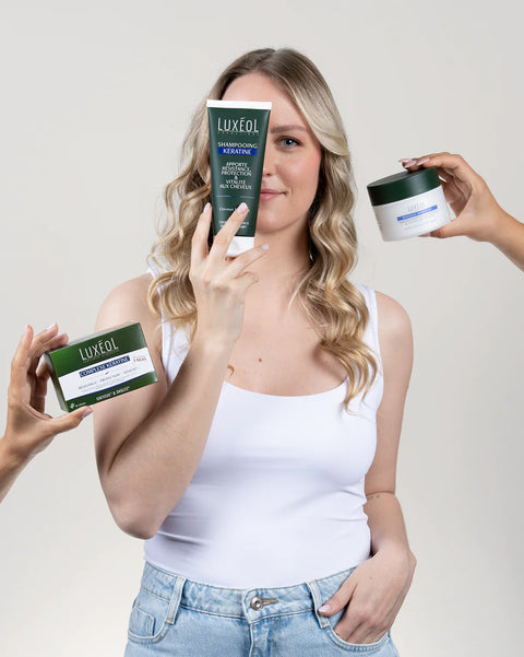 Woman holding Luxeol hair care products against a plain background