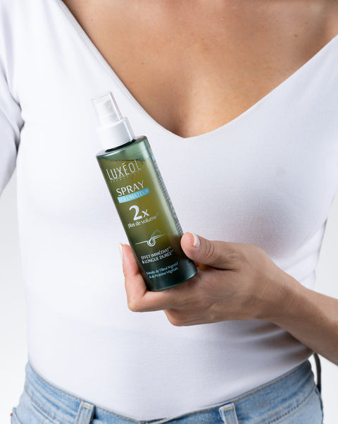 Человек держит бутылку спрея Luxe Oil на белом фоне